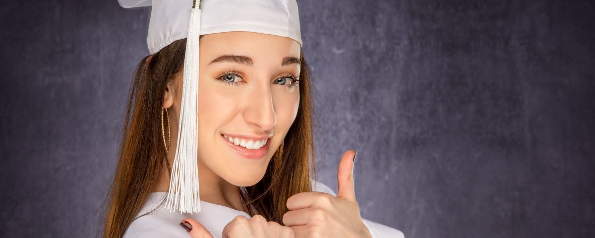 Senior picture of girl in white cap and gown on a gray background